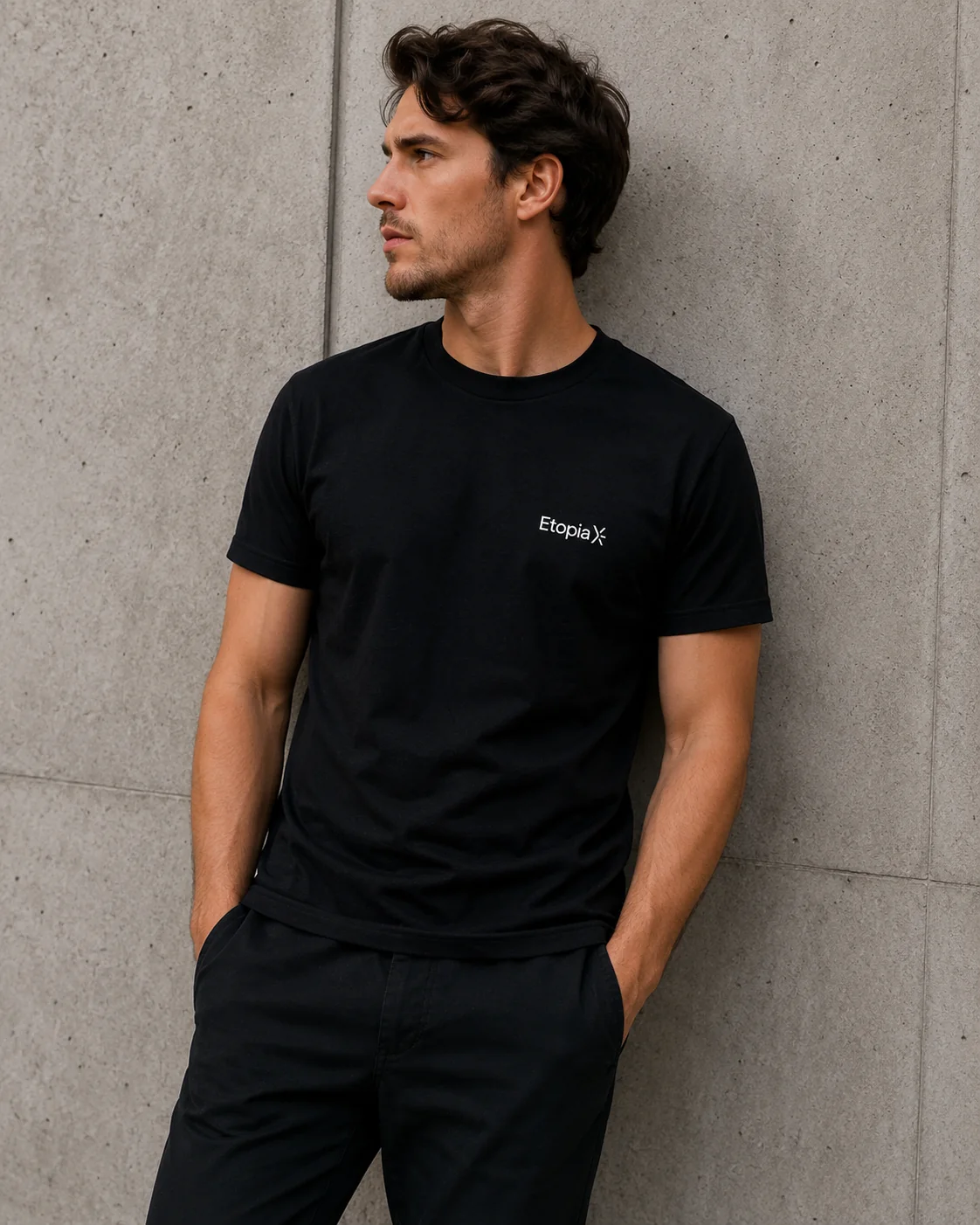 Le t-shirt noir EtopiaX porté par un homme, adossé à un mur de béton