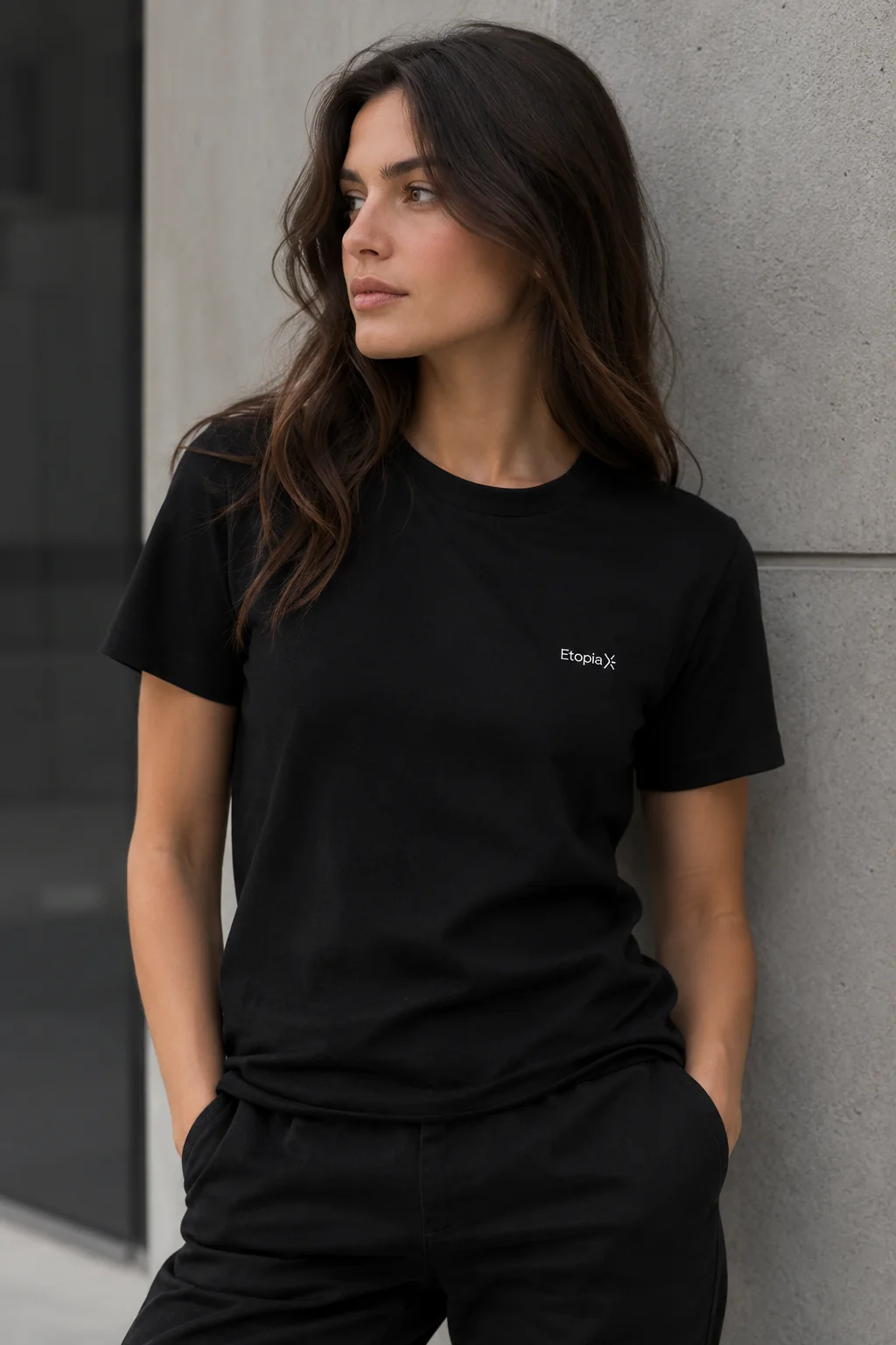Le t-shirt noir EtopiaX porté par une femme, adossée à un mur de béton