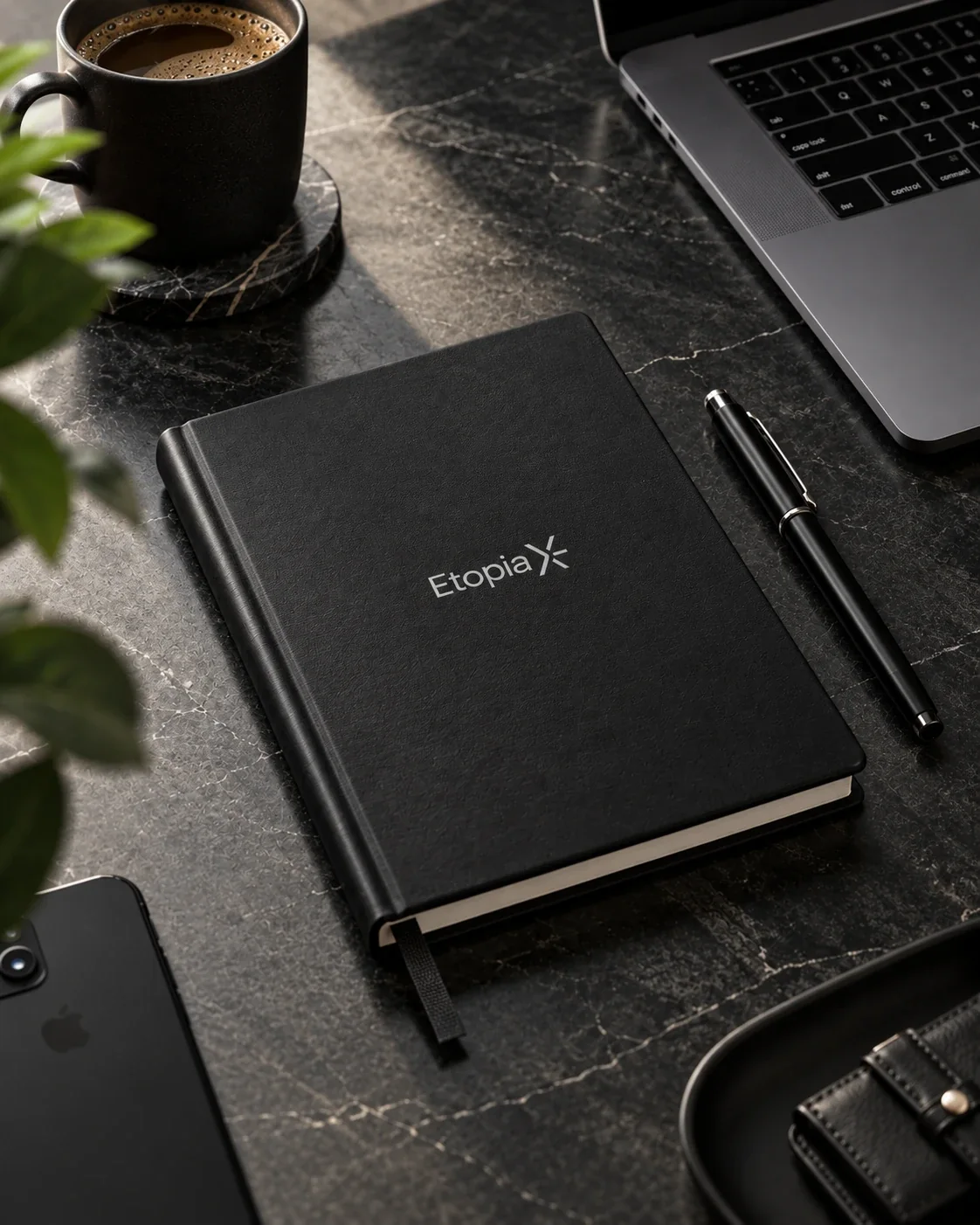 Le carnet noir EtopiaX posé sur un bureau de marbre noir, à côté d’un stylo et d’un café