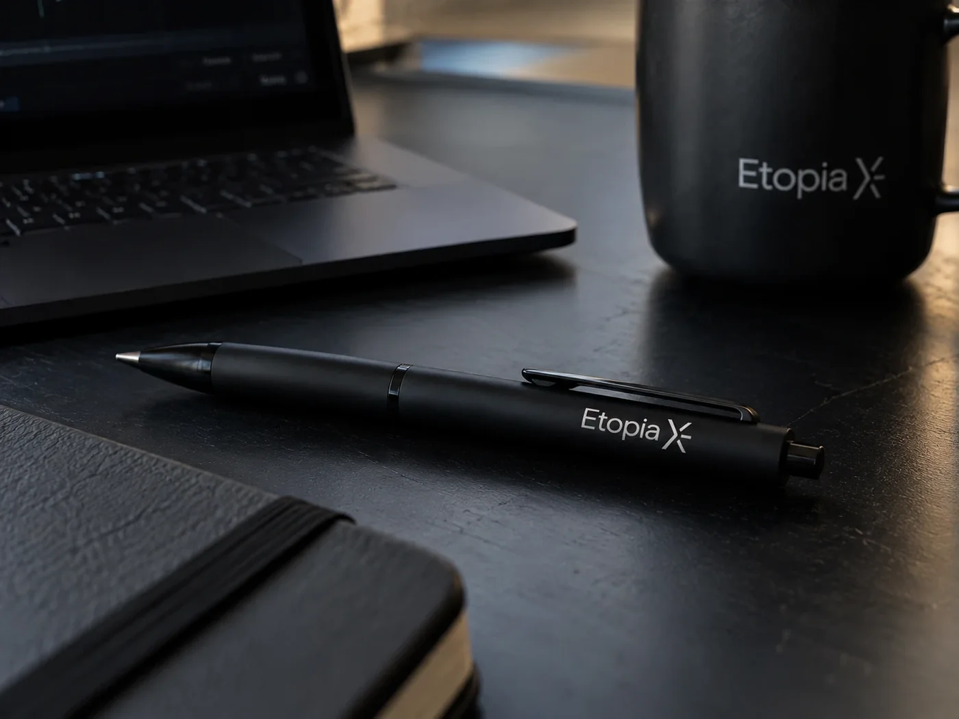 Le stylo noir EtopiaX posé sur un bureau sombre, devant un ordinateur portable
