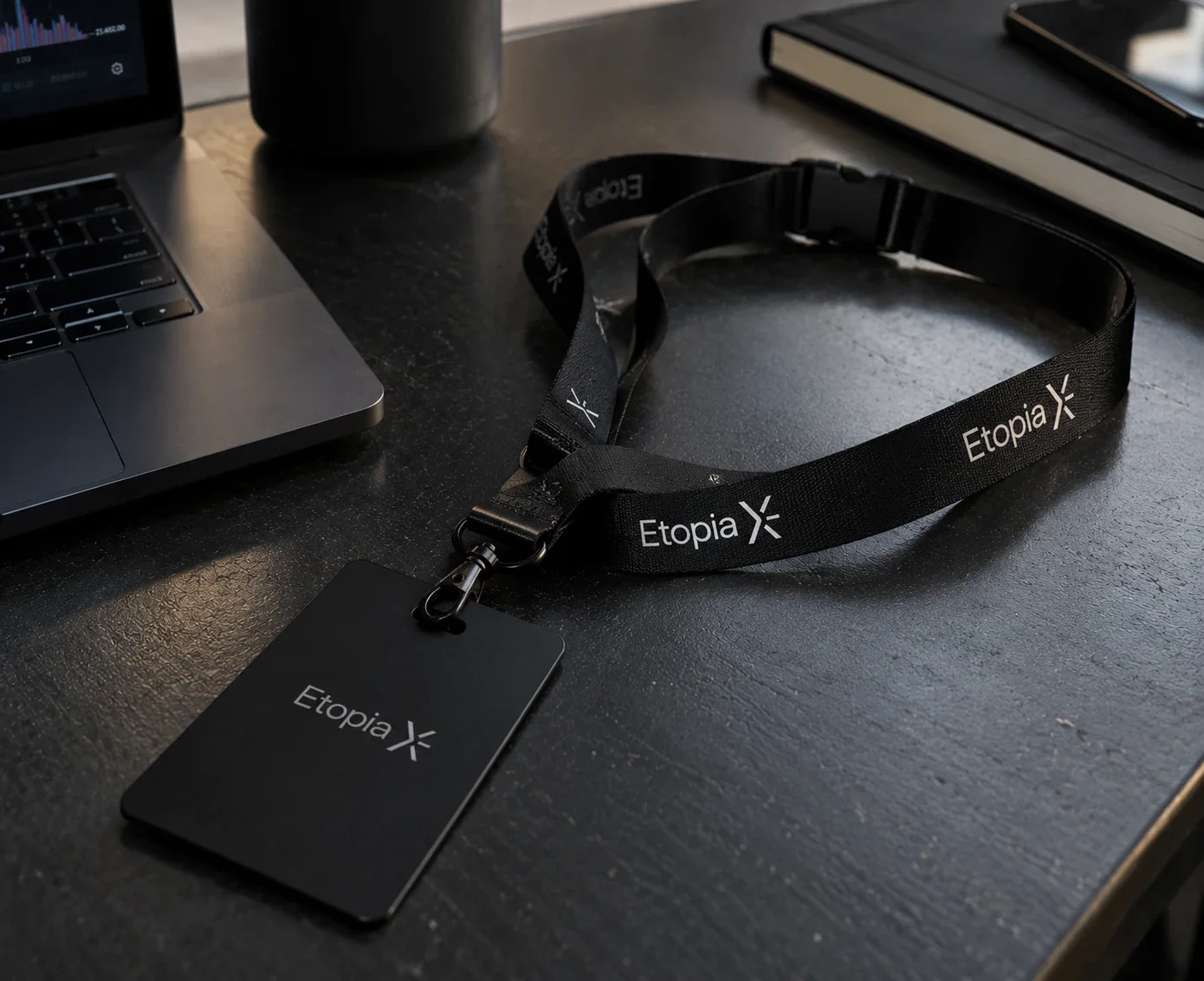Le tour de cou noir EtopiaX et son badge, posés sur un bureau sombre